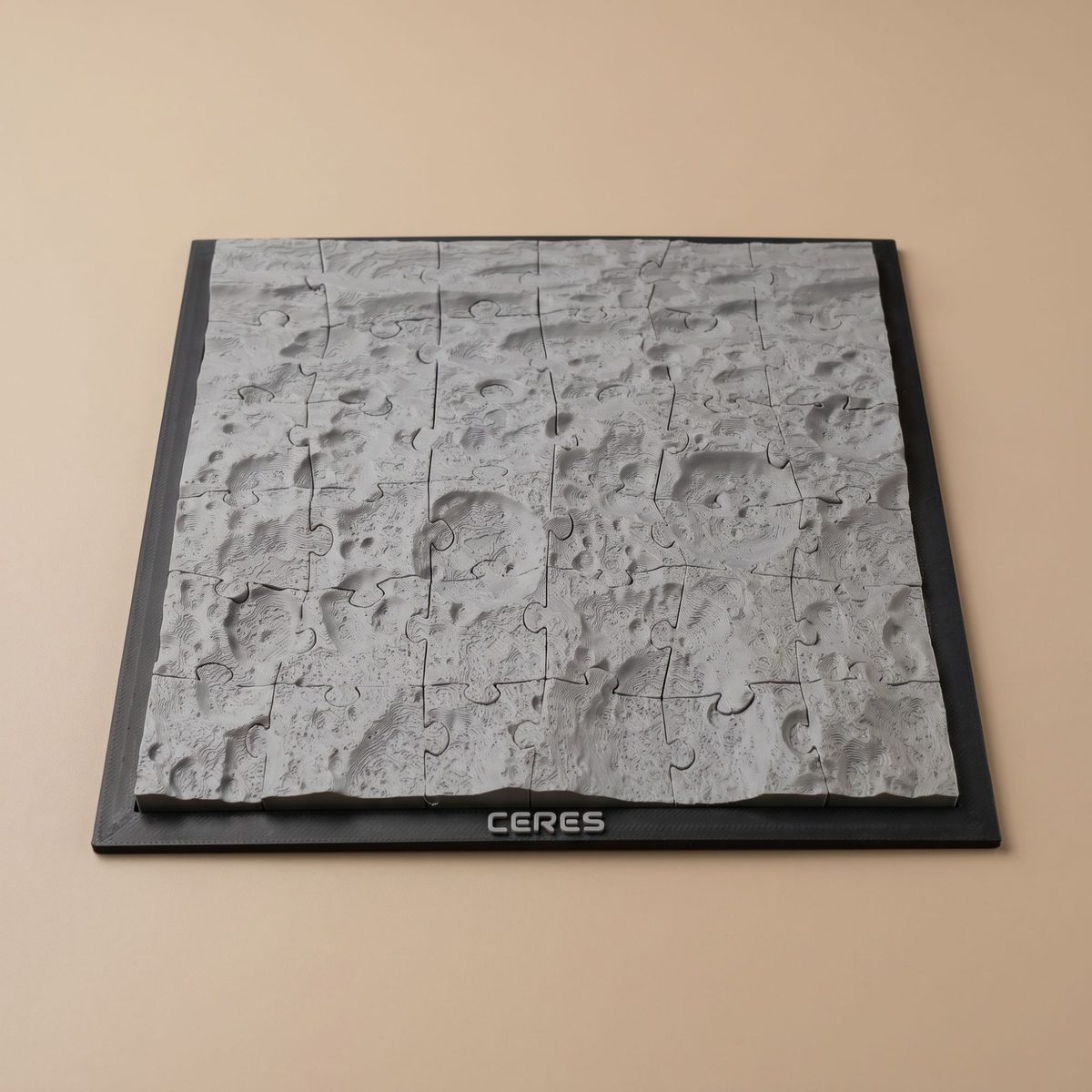 A photo of a printed square Ceres terrain jigsaw puzzle on a black frame lettered CERES