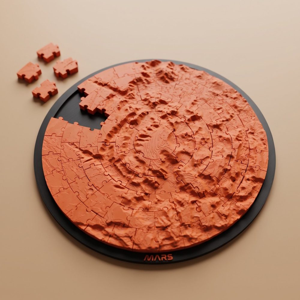 A round Mars terrain jigsaw puzzle in red on a black frame lettered MARS, with four pieces lifted out and lying beside it