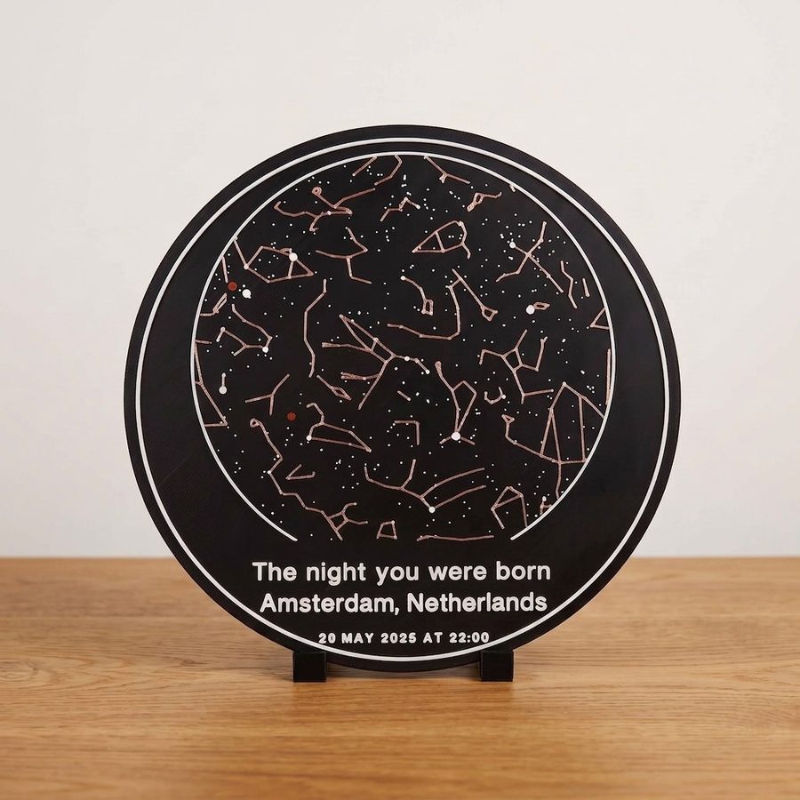 A round StellarMesh star chart plate on a small black desk stand: copper constellation lines, white stars and two red planet dots on a dark plate, lettered The night you were born, Amsterdam, Netherlands, 20 May 2025 at 22:00