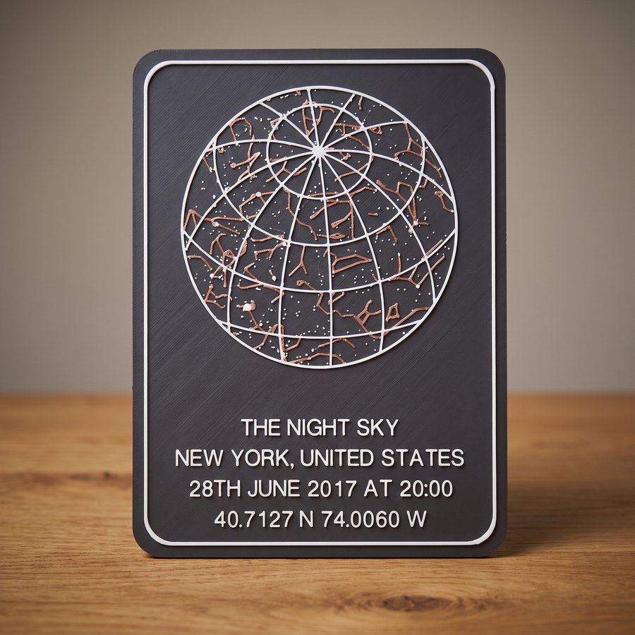 A 3D-printed StellarMesh star chart standing on a wooden desk: a dark grey plate with a white border, the constellation lines picked out in copper filament, and THE NIGHT SKY / NEW YORK, UNITED STATES / 28TH JUNE 2017 AT 20:00 / 40.7127 N 74.0060 W raised in white across the lower half.